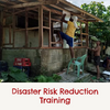 A man standing on a chair to put a piece of tarp up on a house with the caption ' disaster risk reduction training'